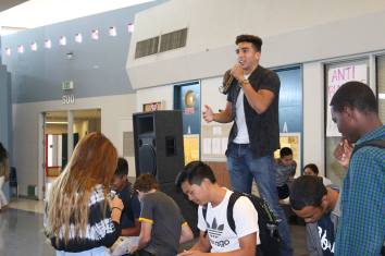 Emcee Anthony Lopez (12) explains the significance of the lunchtime activity in the rotunda while David Lee (11), Austin Beard (12), and two other students squeeze toothpaste onto plates to model the permanence of hurtful words and actions on Friday, October 9, 2015. 